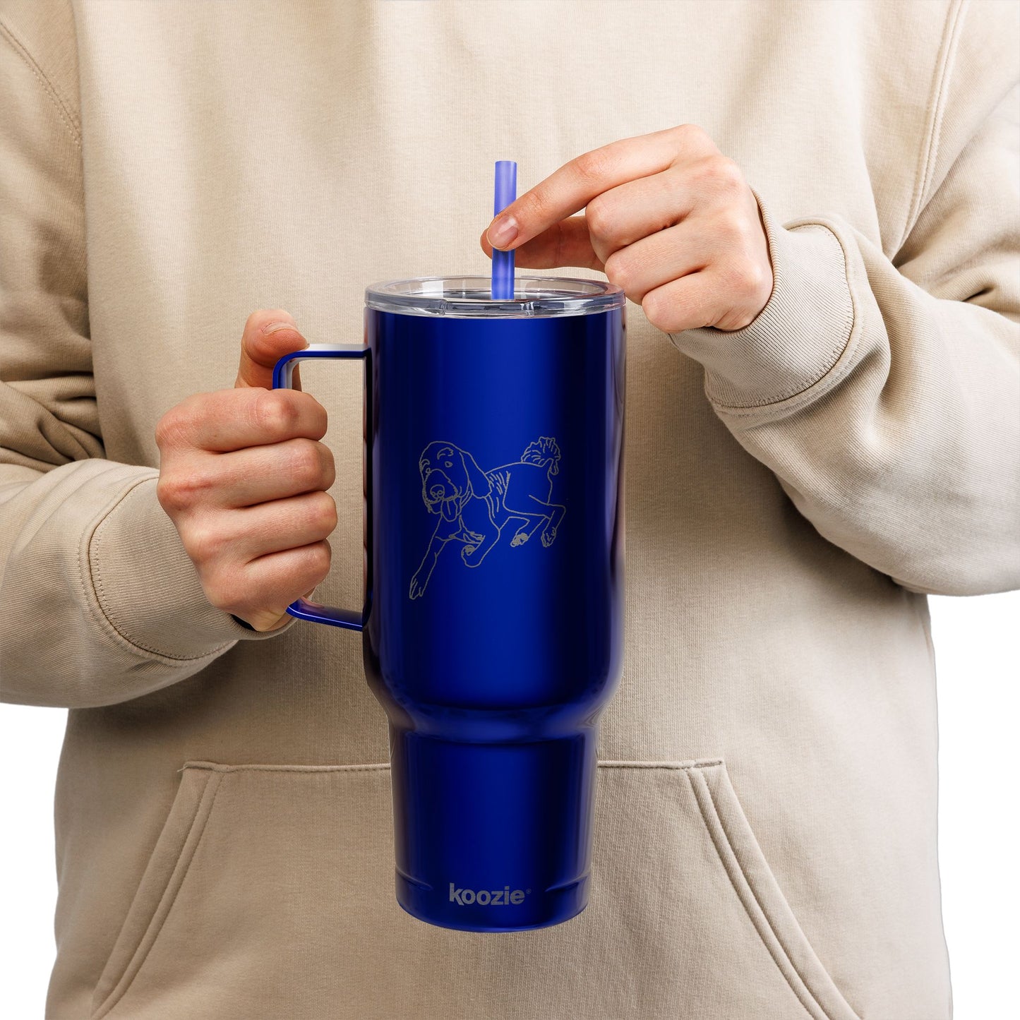 Person holding a blue insulated mug with a straw, wearing a beige hoodie.