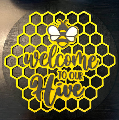 Decorative sign with honeycomb pattern, bee, and 'Welcome to our Hive' text on a dark background.