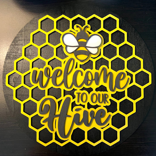 Decorative sign with honeycomb pattern, bee, and 'Welcome to our Hive' text on a dark background.