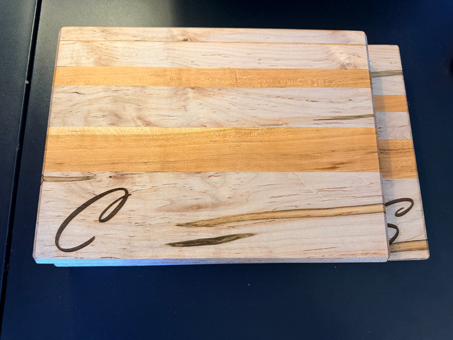 Handcrafted ambrosia maple and cherry wood cutting board with natural grain patterns and engraved initial, edge grain design with smooth finish two size view.