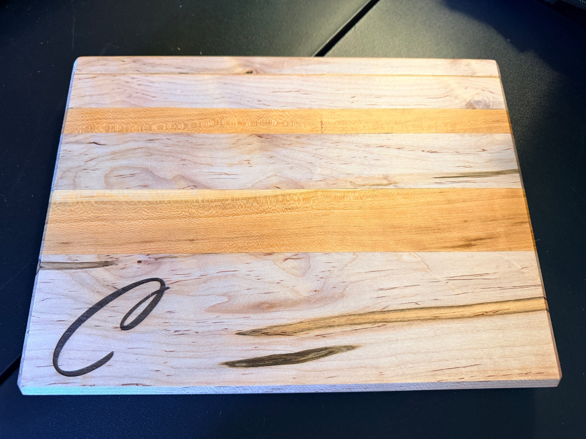 Handcrafted ambrosia maple and cherry wood cutting board with natural grain patterns and engraved initial, edge grain design with smooth finish