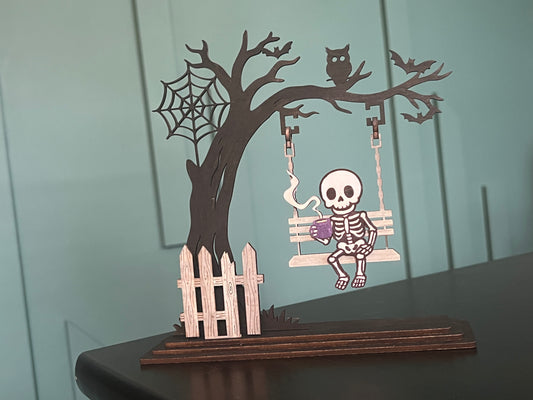 Handmade laser-cut Halloween skeleton décor – spooky skeleton sipping coffee on a swing. Freestanding, hand painted & customizable.
