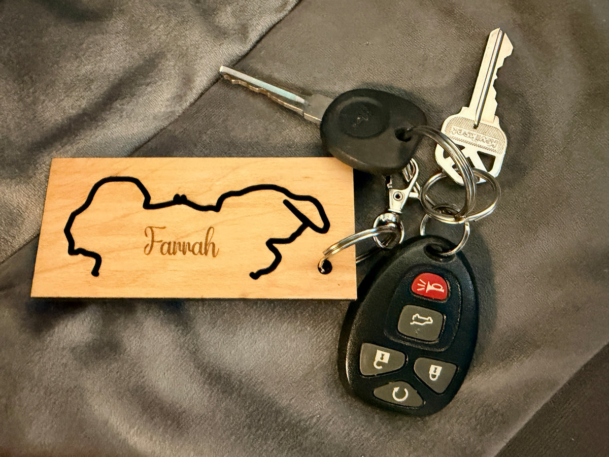 wooden pet keychain engraved with a custom dog outline and the name Farrah,  with a silver key ring on a ring with a set of keys.
