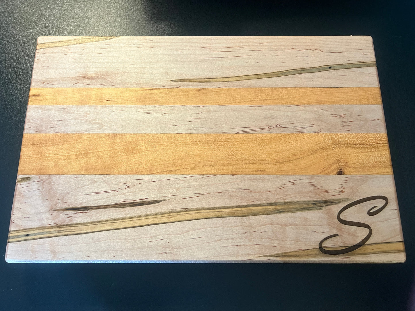 Handcrafted ambrosia maple and cherry wood cutting board with natural grain patterns and engraved initial, edge grain design with smooth finish