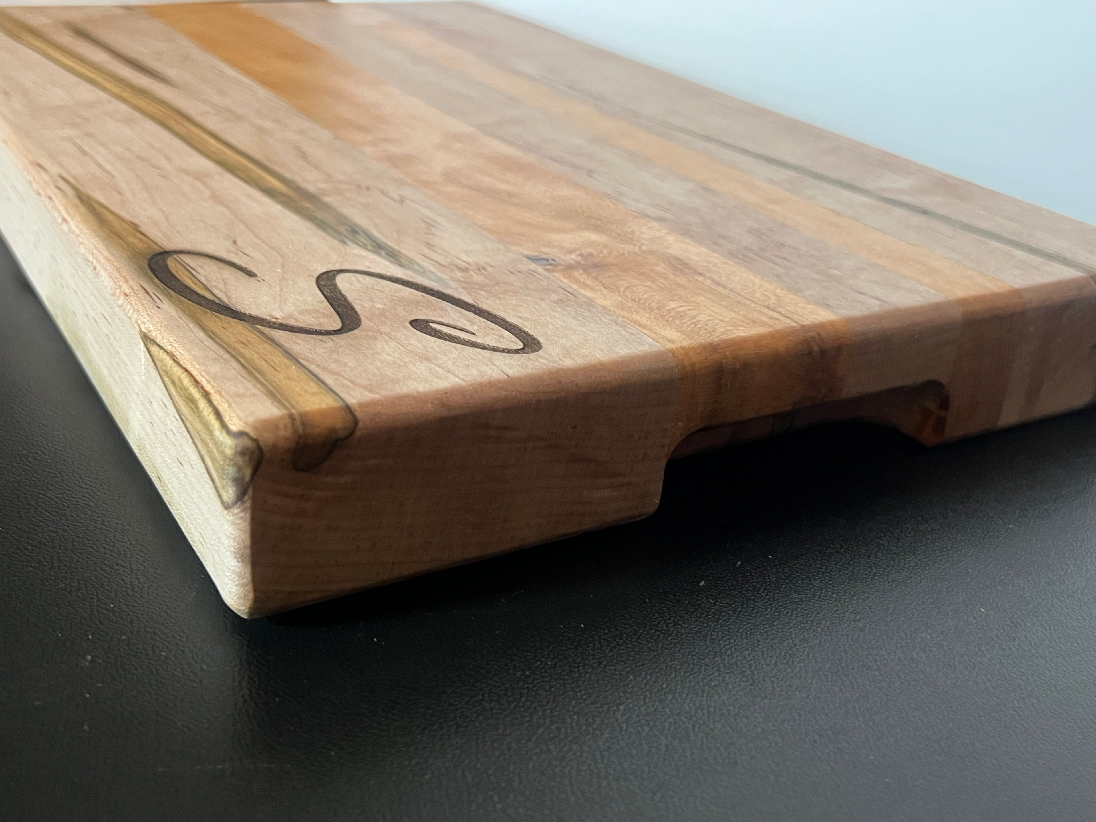 Side view of ambrosia maple and cherry cutting board showing edge grain construction and built-in side handles