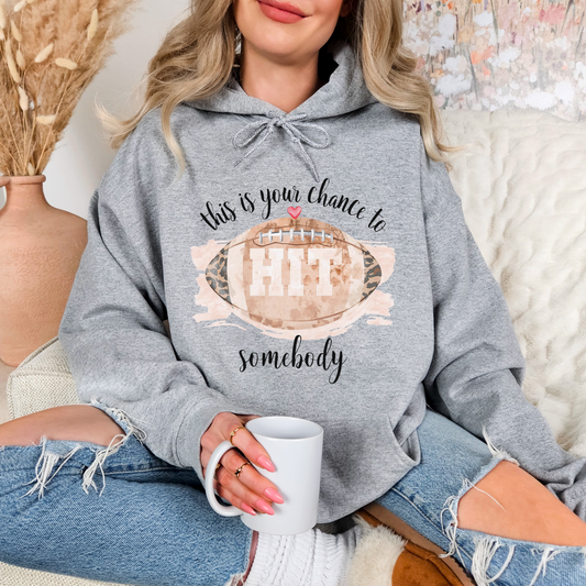 Person wearing a gray hoodie with a football graphic and text, holding a white mug.