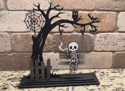 Handmade laser-cut Halloween skeleton décor – spooky skeleton sipping coffee on a swing. Freestanding, hand painted & customizable.

